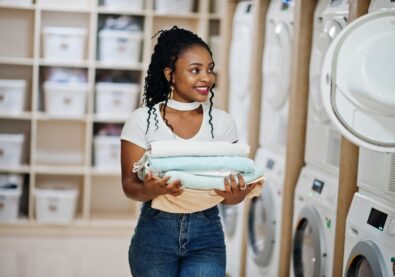 Cheerful african american woman with towels in hands near washing machine in the self-service laundry.