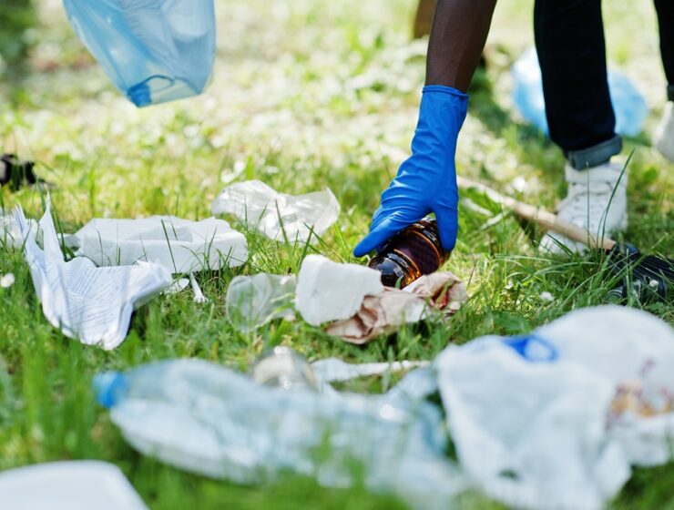 Hand of african american man picking up bottle into garbage bags while cleaning area in park. Africa volunteering, charity, people and ecology concept.
