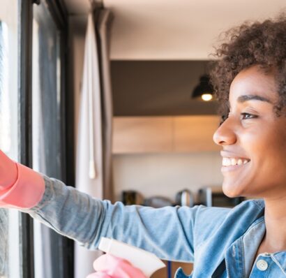 Portrait of young afro woman in gloves cleaning window with rag at home. Housework, housekeeping and cleaning concept.