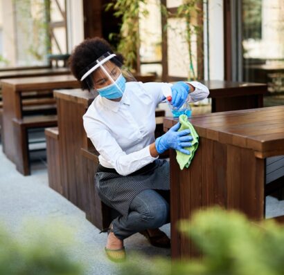 African American waitress disinfecting tables at outdoor cafe during coronavirus epidemic.