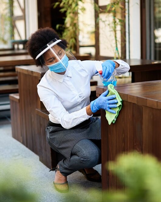 African American waitress disinfecting tables at outdoor cafe during coronavirus epidemic.