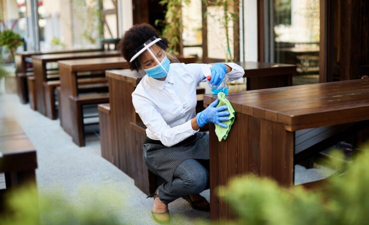 African American waitress disinfecting tables at outdoor cafe during coronavirus epidemic.