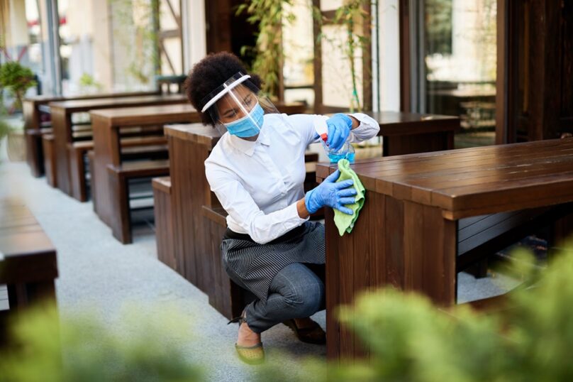 African American waitress disinfecting tables at outdoor cafe during coronavirus epidemic.